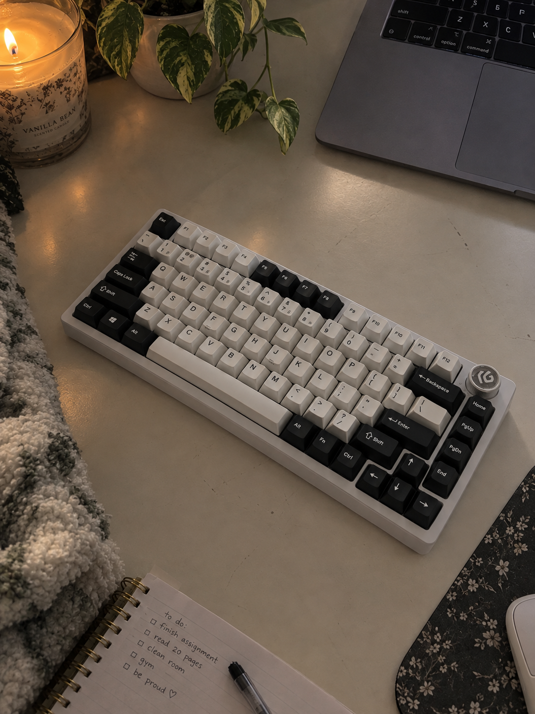 A KeebsforWater black and ivory custom keyboard on a warm desk beside a candle and plant